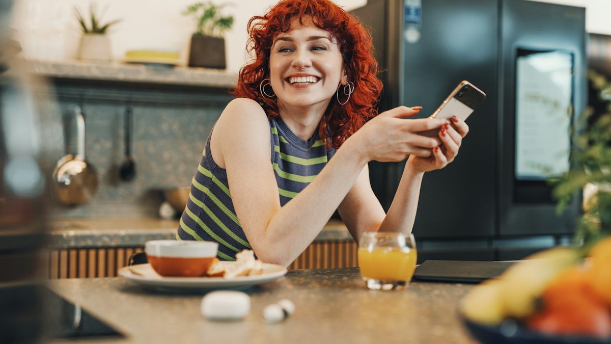 Smiling woman using her phone at the kitchen counter