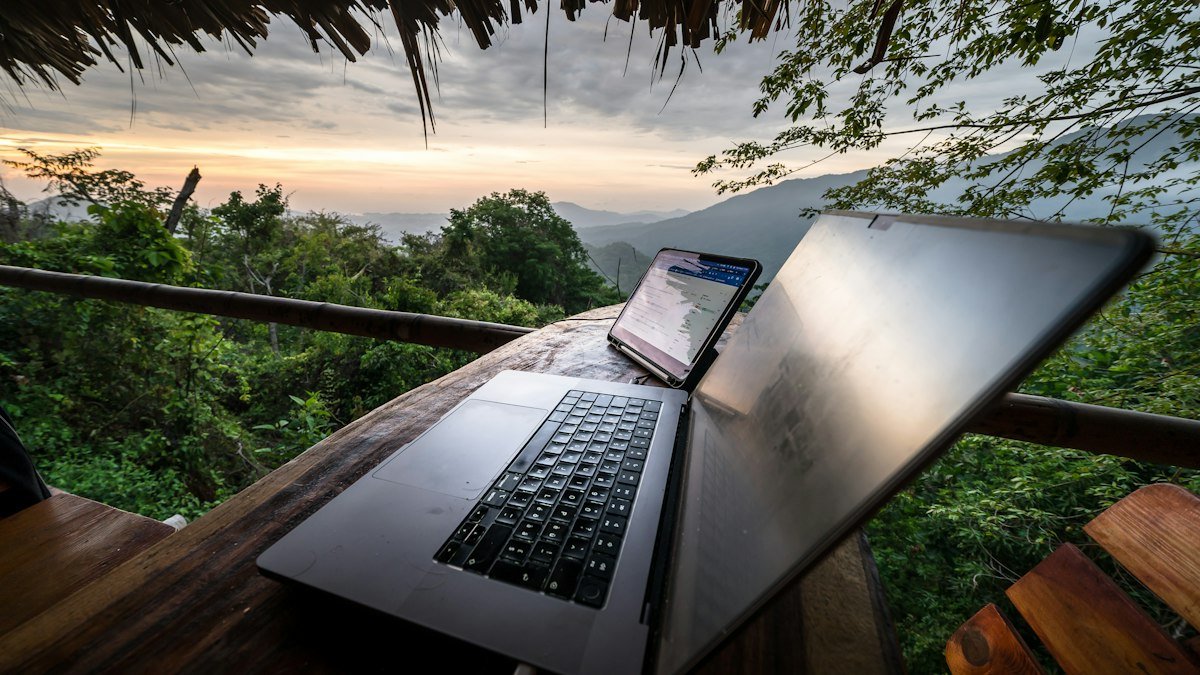 Laptop and tablet on a wooden table overlooking forested hills